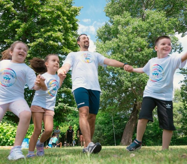 Group of joyful children playing outdoors with an instructor in a sunny park.